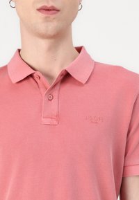 Roze polo shirt met een kraag en een twee-knopen sluiting. Heeft een subtiele, ingeslagen "JOOP!" logo op de linkerkant van de borst. Zachte stofstructuur.