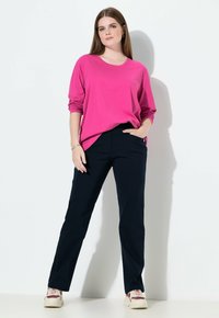 Długi rękaw koszuli w kolorze fuksji z podwiniętymi rękawami, zestawiony z granatowymi spodniami. Strój cechuje się luźnym krojem i bocznymi kieszeniami, noszony z jasnymi trampkami.