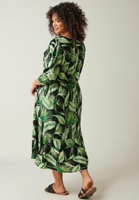 Bloemenmaxi-jurk met een zwarte achtergrond versierd met groene bladdessins. Het heeft lange mouwen, een aansluitende taille en een gelaagde zoom.