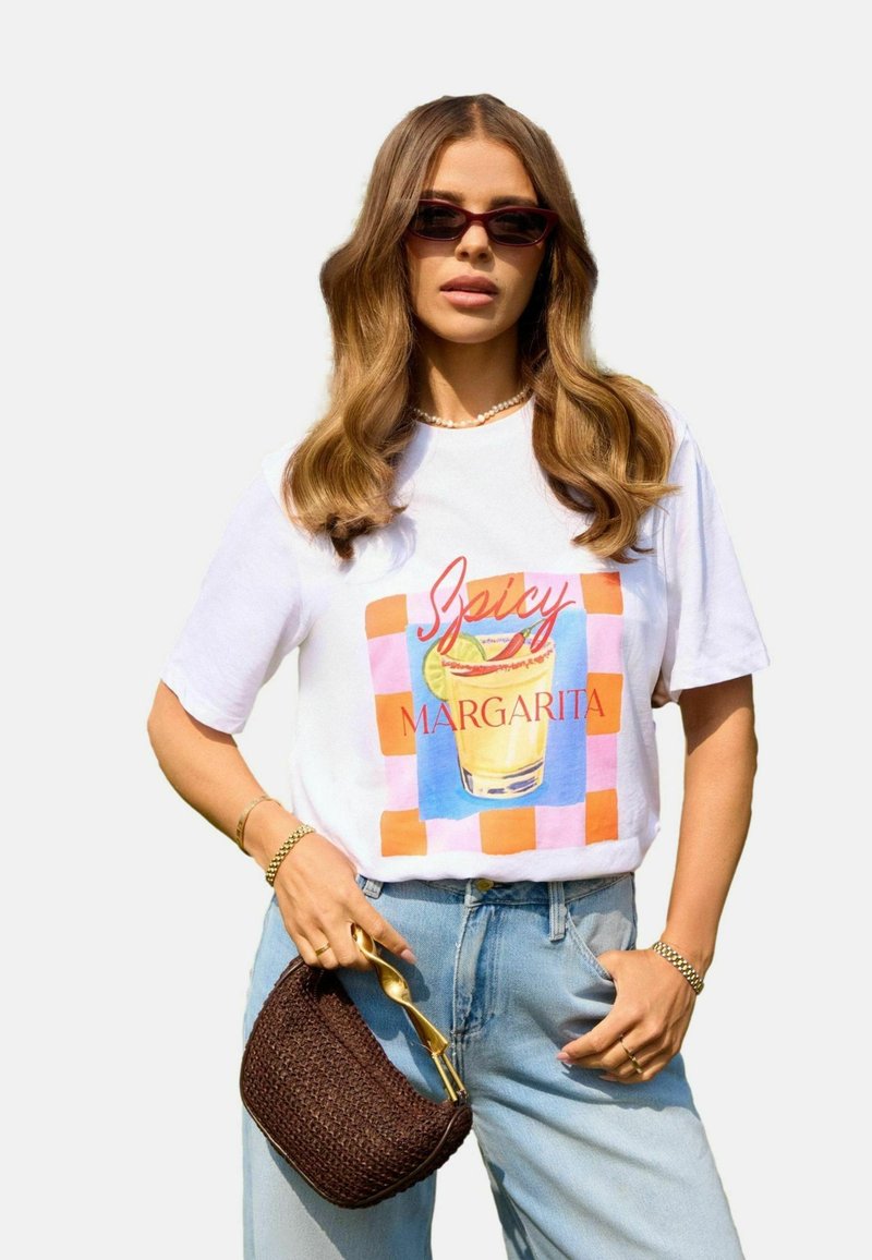 Weißes Grafik-T-Shirt mit buntem "Spicy Margarita"-Druck, kombiniert mit hellblauen Jeans, einer geflochtenen braunen Handtasche und Sonnenbrille.