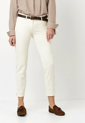 White fitted jeans with side slits at the hem, paired with a striped brown and white blouse and brown shoes. Braided brown leather belt included.