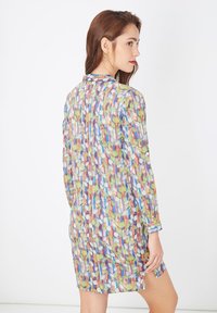 Vestido transparente colorido con un estampado de hojas en azul, verde y rojo, con mangas largas y un corte relajado, que llega a mitad del muslo.