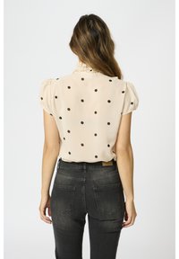 Beige blouse met stippen, korte pofmouwen, een gerimpelde kraag en doorschijnende textuur, gecombineerd met donkergrijze jeans.