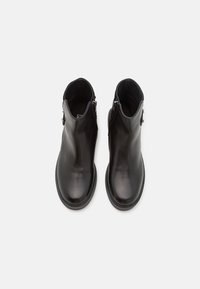 Černé kožené kotníkové boty s hladkou texturou, zaoblenou špičkou a bočními zipy. Plochá podrážka a minimalistický design zvyšují univerzálnost.