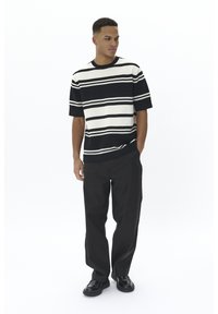 T-shirt en tricot rayé noir et blanc à manches courtes, associé à un pantalon noir ample et des chaussures noires brillantes.