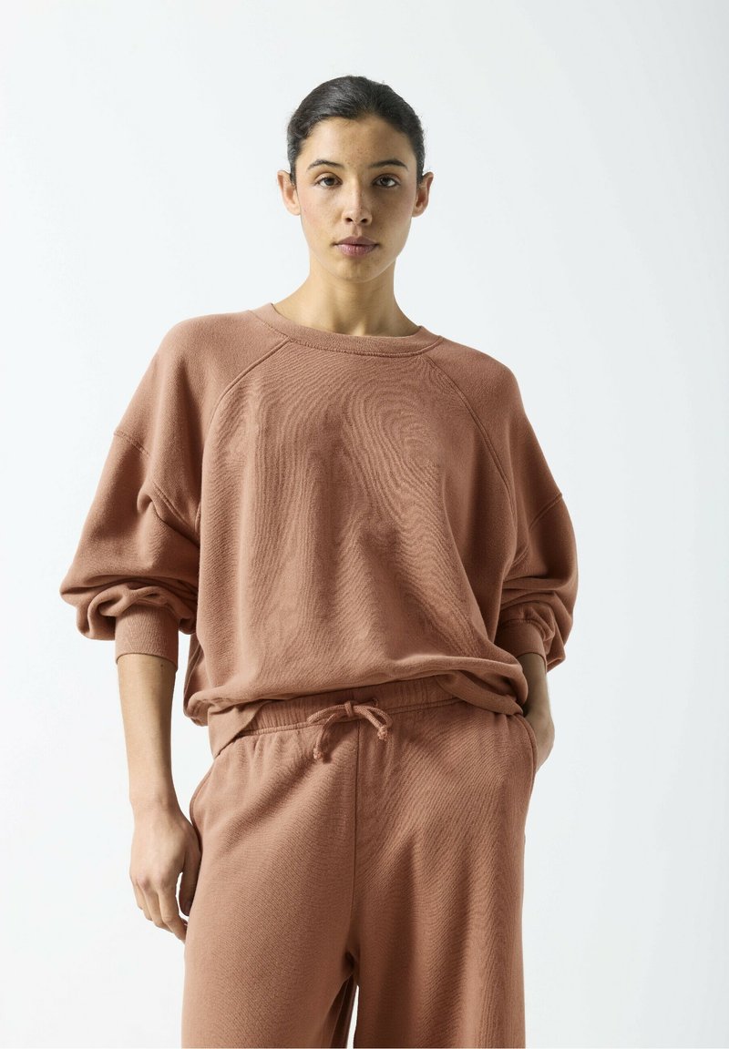 Sweat-shirt ample marron clair avec poignets côtelés, encolure ronde et tissu texturé, associé à un pantalon de survêtement à cordon de serrage assorti.