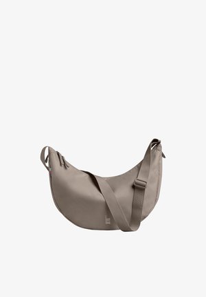 Smukła torebka na ramię w kształcie półksiężyca w kolorze taupe z regulowanym paskiem i zamkiem błyskawicznym, oznaczona logo "GOT BAG" z przodu.