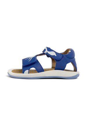 Blå lädersandal med vita accenter och utskärningar, med justerbara velcroremmar och en texturerad vit sula. Avslappnad design.