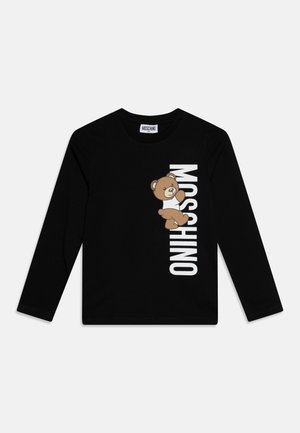 Sort langærmet skjorte med en brun tøjdyrsbjørn iført en hvid skjorte, der klatrer op ad hvid lodret "MOSCHINO" tekst foran.