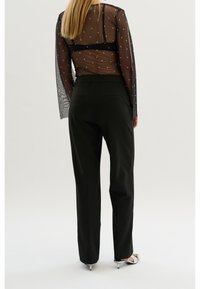 Svarta skräddarsydda byxor i kombination med en genomskinlig svart blus med polka prickar och långa ärmar. Blusen har en figurnära silhuett och en strukturerad design.