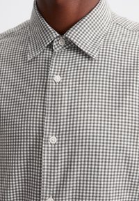 Camicia a scacchi grigia e bianca con colletto a camicia, bottoni bianchi prominenti e un tessuto testurizzato con motivo gingham.