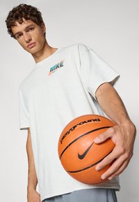 Hvid oversized t-shirt med et flerfarvet Nike-logo, parret med en orange basketball, der viser Nike-logoet og teksten "playground".