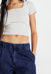 Top corto de canalé gris con escote cuadrado, combinado con pantalones de mezclilla oscuros de tiro alto, que cuentan con bolsillos laterales y pliegues.