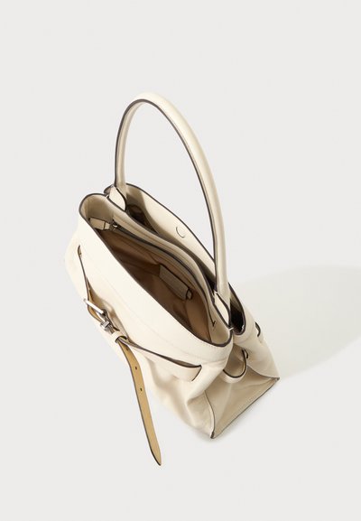 Sac à main en cuir crème avec détail boucle et ouverture supérieure montrant une poche intérieure zippée, sur un fond clair uni.