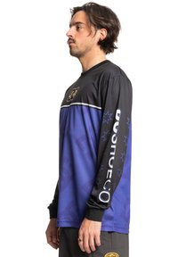 Atletska majica s long sleeves, s crnim gornjim dijelom i gradijentnim ljubičastim donjim dijelom. Prikazuje logotipe, pruge i uzorke zvjezdica duž rukava.