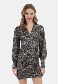 Leopardprintkjole med lange ærmer, dyb v-hals, samlet tekstur og tætsiddende silhuet i nuancer af sort og tan.