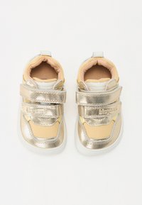 Chaussures pour tout-petits en métal doré avec des accents jaunes et blancs, dotées de straps Velcro et d'un design texturé sur les côtés. Doublure intérieure douce.