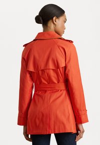 Rode waterdichte trenchcoat met een ceintuur in de taille, schouderepauletten en een rugventilatie. Heeft lange mouwen en een gladde textuur.