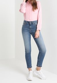 Light pink button-up shirt, blue high-waisted jeans, and white chunk-soled sneakers, creating a casual outfit. Smooth texture, fitted design.