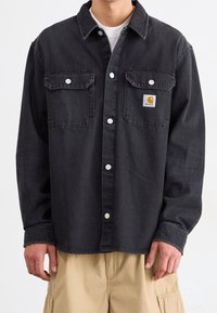 Black denim shirt with two chest pockets, white snap buttons, and a small square logo tag on the left pocket. Long sleeves.