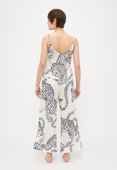 Sleeveless jumpsuit in white fabric featuring a leopard print in black and blue. Loose fit, wide legs, with subtle texture and open back design.