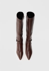 Par de botas de cuero marrón hasta la rodilla con puntera afilada y cremallera lateral, vistas desde arriba sobre un fondo gris liso.