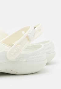 Fehér Crocs szandálok, textúrált gumitalppal, állítható keresztpánttal, logóval, és sima, kerek formával.