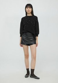 Czarny sweter dzianinowy z perłowymi akcentami, w połączeniu z czarną mini spódnicą z ekoskóry. Modelka nosi przezroczyste czarne skarpetki i czołgające czarne baleriny z ćwiekami.