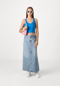 Modrá bezrukávová crop top, svetlomodrá džínová maxi sukňa s vysokým pásom, biele tenisky a ružová kabelka. Námestkové biele slnečné okuliare ako doplnok.