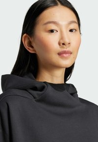 Crna dukserica s visokim, drapiranim izrezom. Mekana tkanina s glatkom teksturom, s minimalnim šavovima i opuštenim krojem.