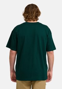 Camiseta de algodón verde con cuello redondo y mangas cortas, mostrada desde la parte de atrás. Textura suave con un corte relajado.
