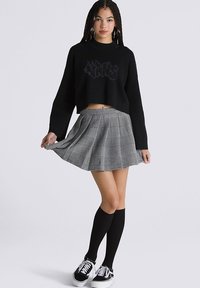 Suéter negro corto con letras en relieve, combinado con una falda plisada gris a cuadros. Medias altas negras y zapatillas negras completan el look.