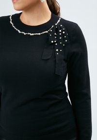 Schwarzer Pullover mit Rundhalsausschnitt, verziert mit einem Kragen aus Perlen und Strasssteinen sowie einer Stoffschleifenakzent auf der linken Schulter.