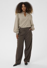 Beež pluus lühikese krae ja puhvärkidega varrukatega, koos pruunide kõrge vöökohaga, volditud pükste ja mustade terava nina kingadega, mis lõpetavad välimuse.