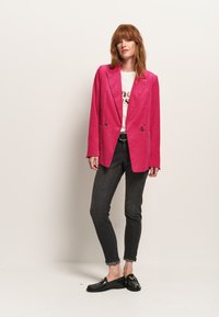 Blazer in corda rosa con design doppiopetto, revers a punta, tasche applicate, abbinato a pantaloni skinny scuri e mocassini neri.