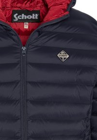 Veste matelassée bleu marine avec un design matelassé horizontal, doublure rouge, fermeture éclair argentée et un écusson logo en forme de losange sur la poitrine.