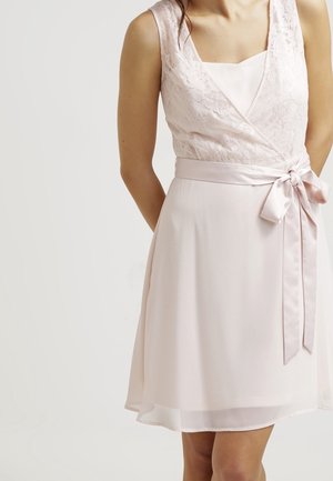 Ärmelloses, hellrosa Kleid mit Spitzenoberteil, V-Ausschnitt und einer Taillenschärpe, die rechts zu einer Schleife gebunden ist.