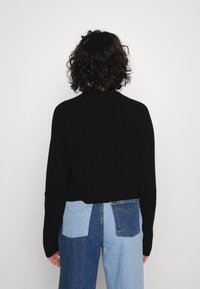 Czarny prążkowany sweter dziany z wysokim kołnierzem i rękawami raglanowymi, noszony na niebieskich dżinsach typu patchwork, prezentujących różne odcienie i faktury.