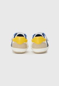 Vista posteriore di sneaker multicolori con materiali blu, bianchi, gialli e beige, dotate di una fibbia in velcro e design della punta arrotondata.
