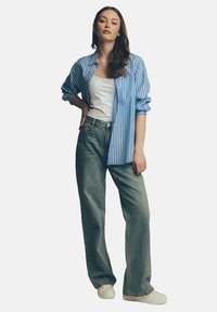 Niebieska i biała w paski koszula zapinana na guziki noszona na białym topie na ramiączkach, w połączeniu z luźnymi jasnoniebieskimi dżinsami i białymi trampkami. Wygodny, codzienny styl.