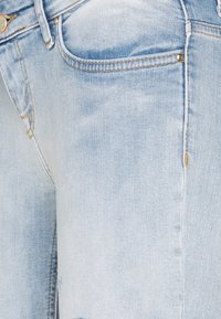 Ljusblå denimjeans med en blekt finish, utrustad med en klassisk femfickdesign, synlig sömnad och metallnitar.