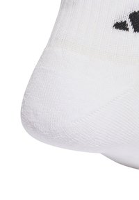 Calcetín deportivo blanco hecho de tela texturizada, con una zona acolchada en la punta y un acento de logo negro cerca de la parte superior.