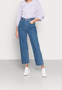 Lyse lilla gingham bluse med en stor krave, parret med højtaljede, vide blå jeans og hvide sneakers.
