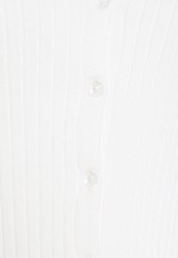 Gros plan sur un tissu blanc côtelé avec deux boutons translucides cousus en ligne verticale.