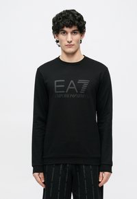 Must pikkade varrukatega dressipluus ümmarguse kaelusega ja toonitoonis "EA7 Emporio Armani" logoga ees. Pehme kangas, sileda tekstuuriga.