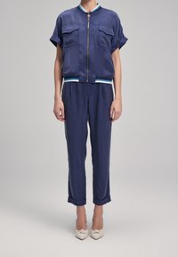 Granatowy, dwuczęściowy zestaw składający się z kurtki z krótkim rękawem z zamkiem błyskawicznym i dwiema kieszeniami oraz dopasowanych spodni zwężanych na końcu; oba wykonane z teksturowanej tkaniny.