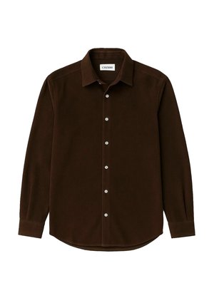 Brun kordflorskjorta med spetsig krage, knappslå fram och långa ärmar. Har en subtil ribbad struktur och vita knappar.