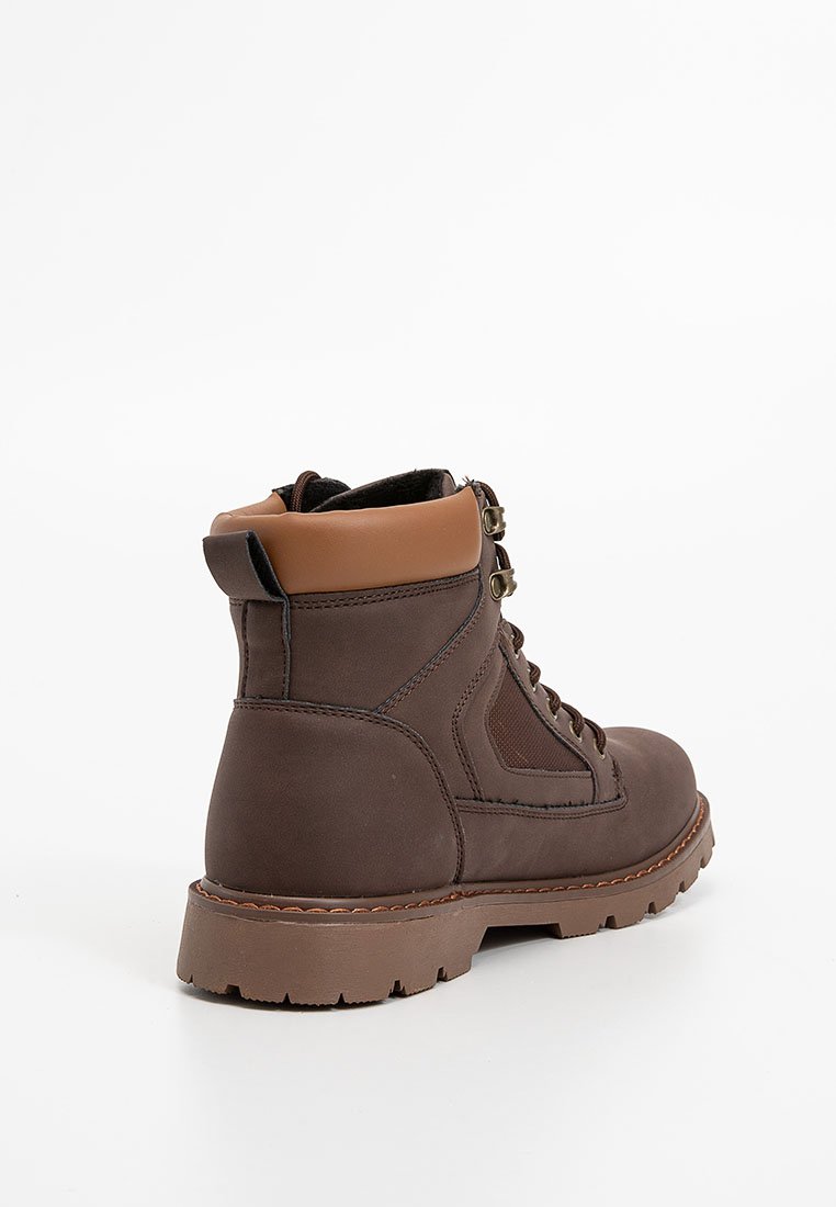 Botas de cuero marrón hasta el tobillo con un collar texturizado en tono beige, cordones en la parte delantera y ojales metálicos. Presenta una suela de goma resistente con patrones de agarre visibles.