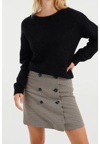 Černý pletený svetr s diagonálním vzorem, doplněný minisukní v psím zubu s černými knoflíky a přiléhavým pasem.