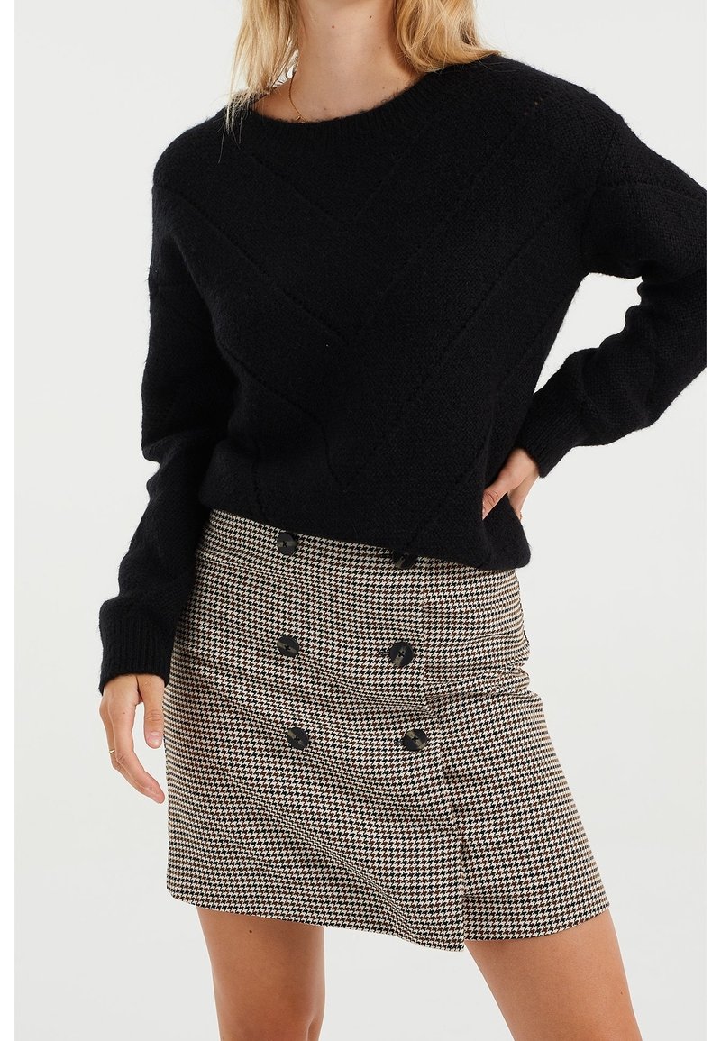 Černý pletený svetr s diagonálním vzorem, doplněný minisukní v psím zubu s černými knoflíky a přiléhavým pasem.